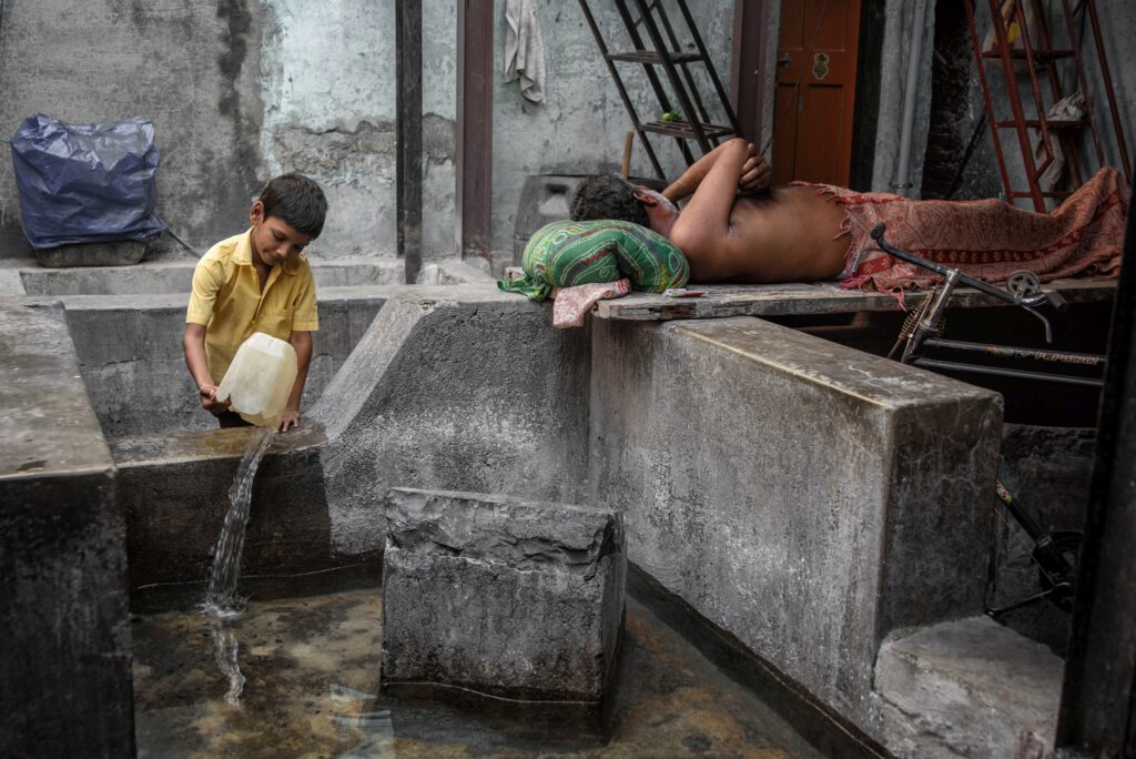 Indyjski chłopiec wylewający wodę przy śpiącym mężczyźnie