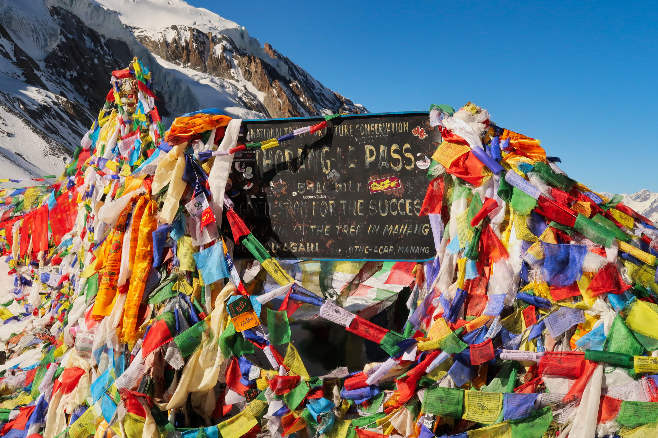 The sign marking the highest point of the Thorong, Thorung, Thorang La pass, covered by hundreds of colorful prayer flags, Annapurna Circuit Trek, Nepal
